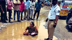 రోడ్డుపై బురద గుంతలో కూర్చుని మహిళ వినూత్న నిరసన