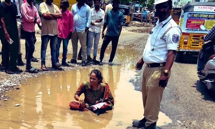 రోడ్డుపై బురద గుంతలో కూర్చుని మహిళ వినూత్న నిరసన